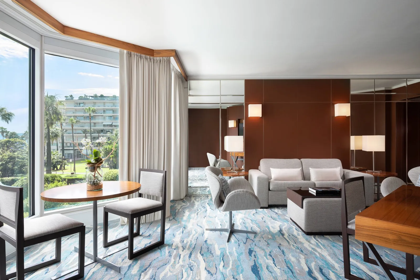 Suite lounge with grey sofas, dining table and floor-to-ceiling windows over Cannes at JW Marriott Cannes