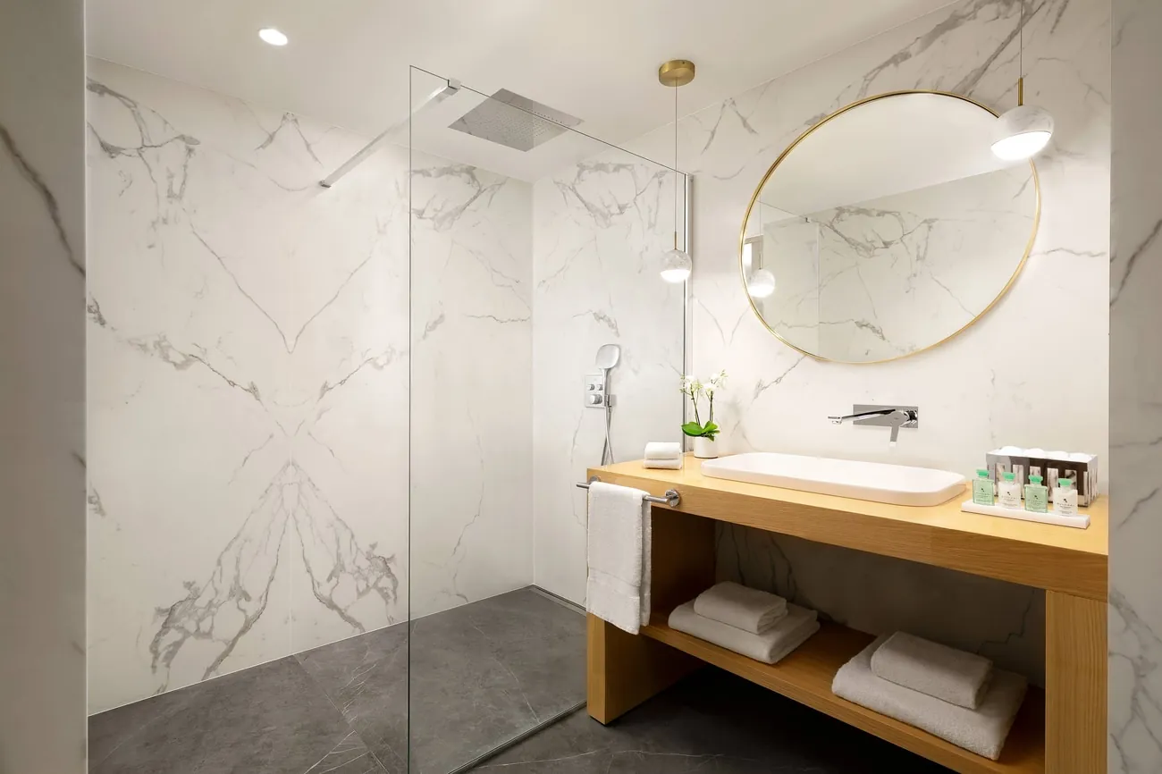 Marble bathroom with walk-in shower, wood vanity and gold-rimmed mirror at JW Marriott Cannes