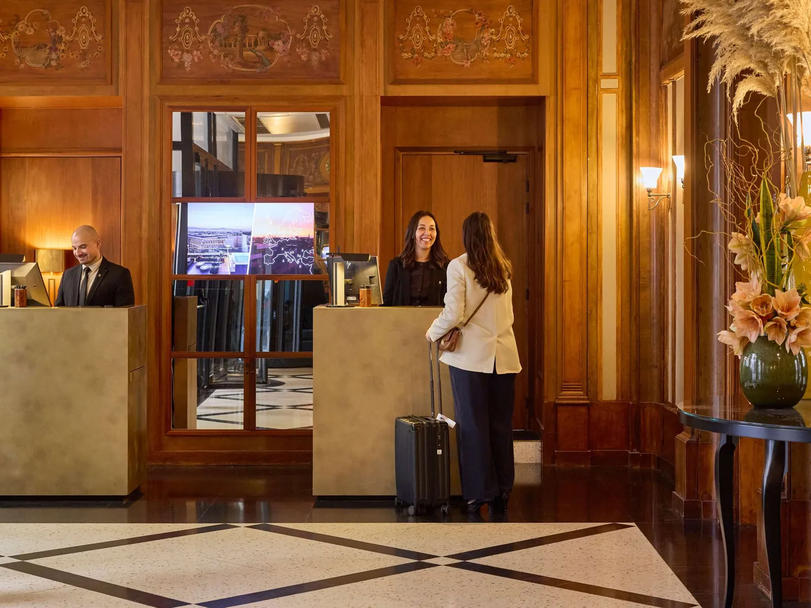 Lobby reception with wood panelling, a marble floor and a guest checking in at L'Echiquier Opéra Paris MGallery