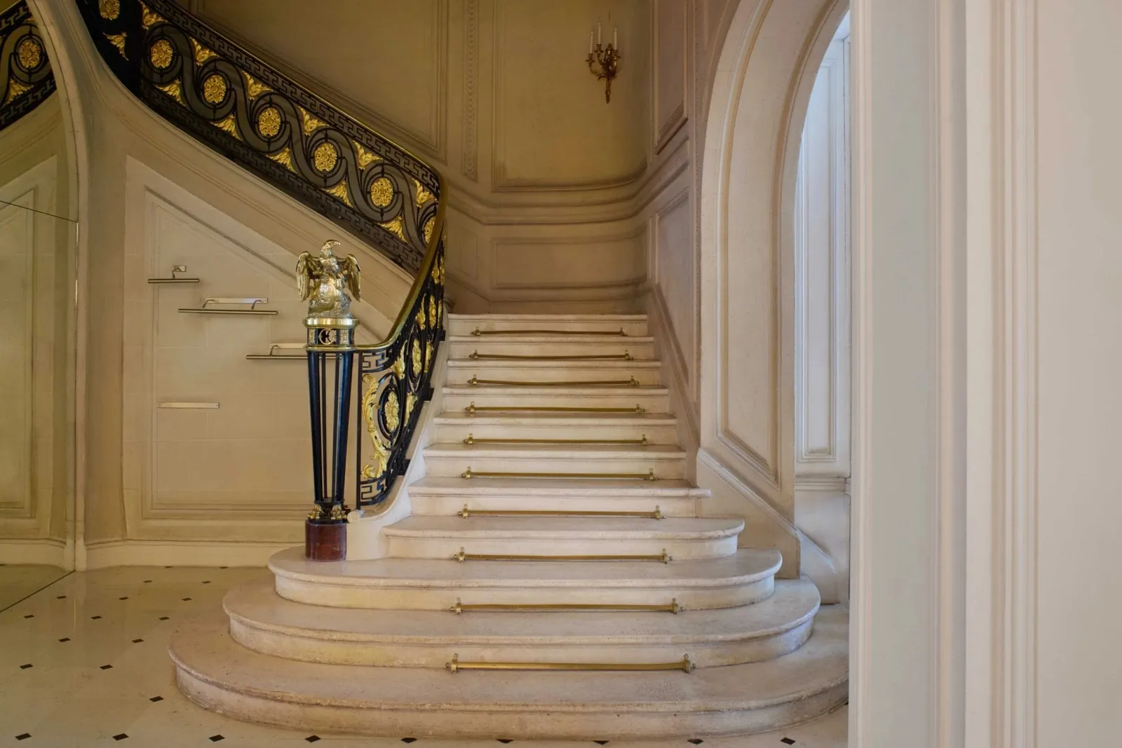 Marble staircase with a gilded wrought-iron balustrade and a golden eagle finial at La Maison Champs-Élysées