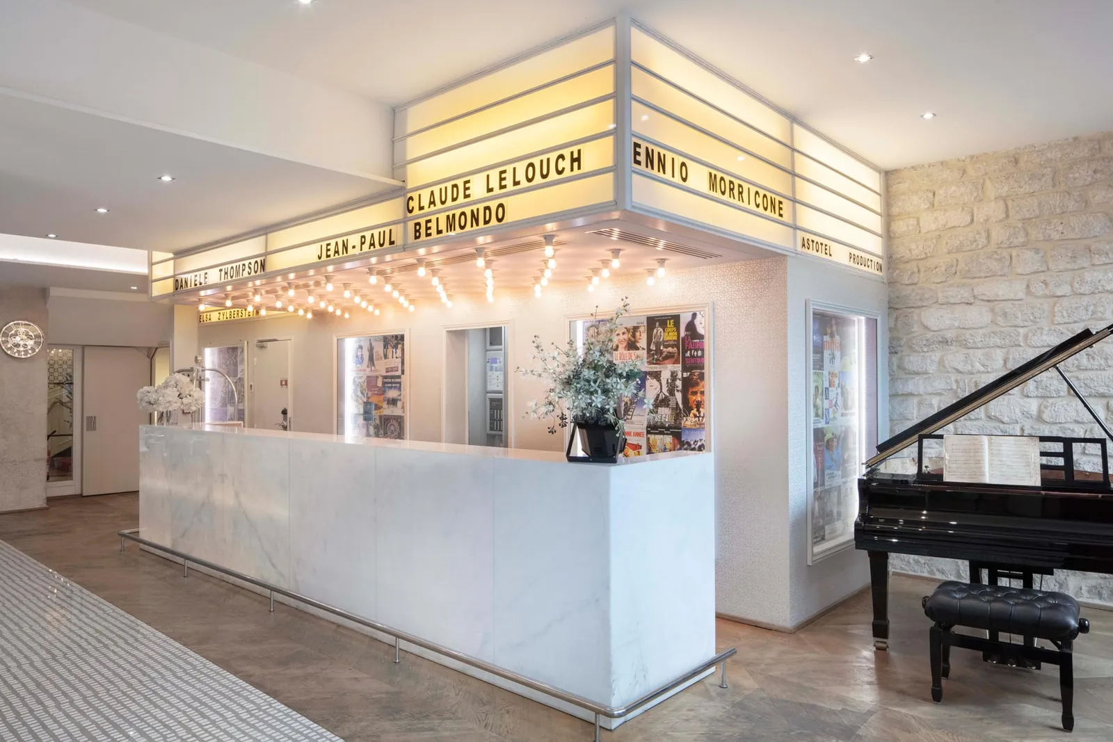 Reception counter under a lit marquee of film names, with a black grand piano beside it at Le 123 Sébastopol
