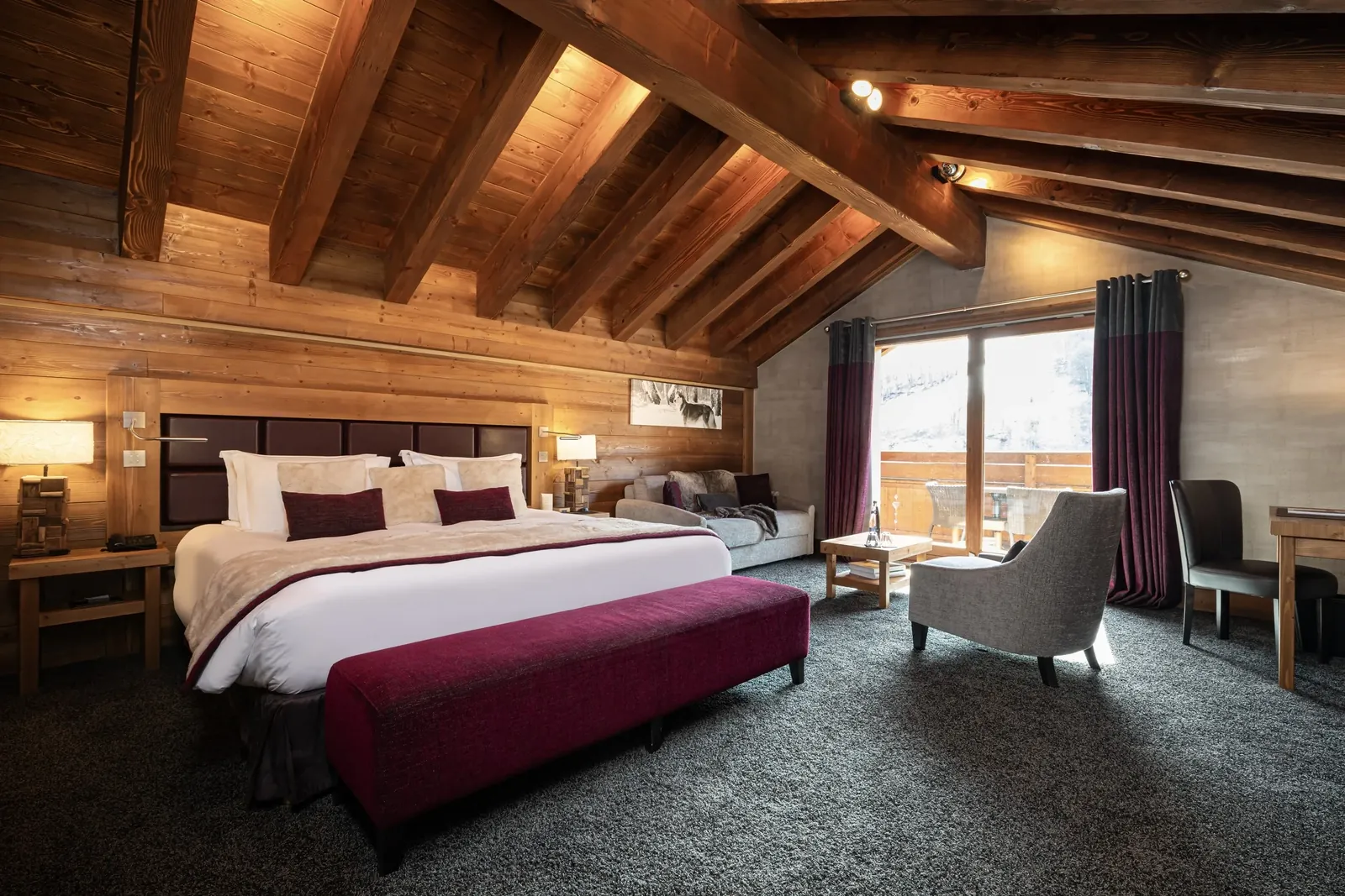 Guest room with exposed timber beams, a burgundy bench and a balcony view at Le Kaïla, Méribel