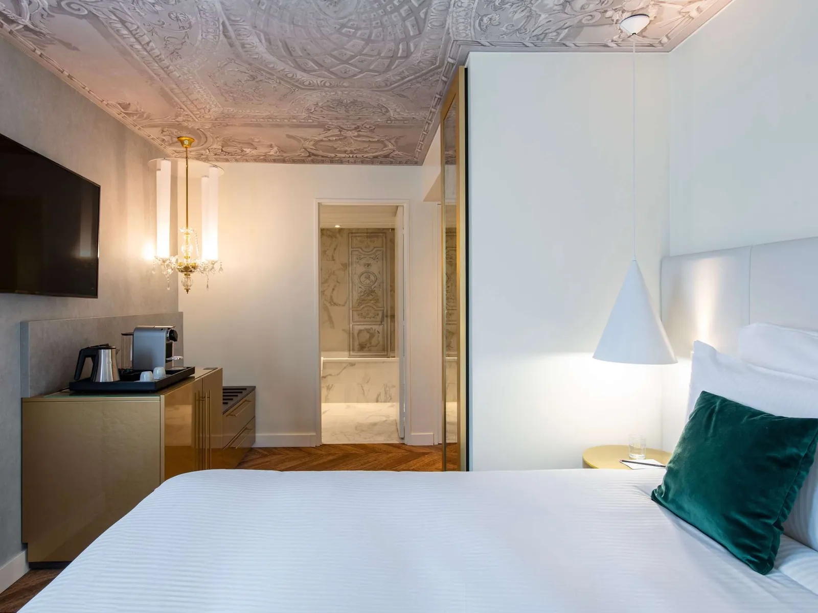 Bedroom with white bedding, dark wood panels and a bedside lamp at Le Louis Versailles, Versailles