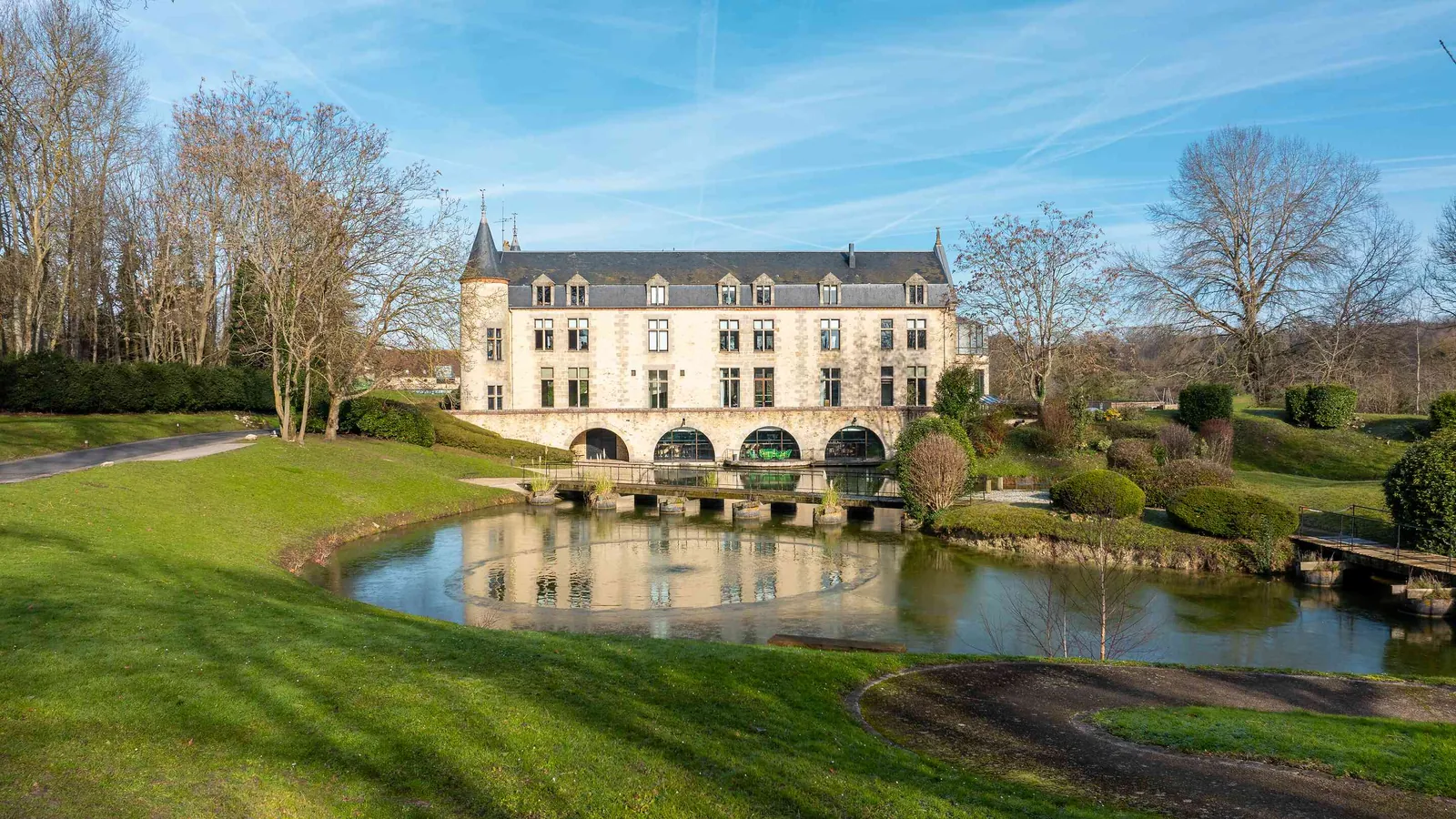Stone building beside a reflecting pond and lawns at Les Lisières du Gâtinais, a seminar campus in Seine-et-Marne