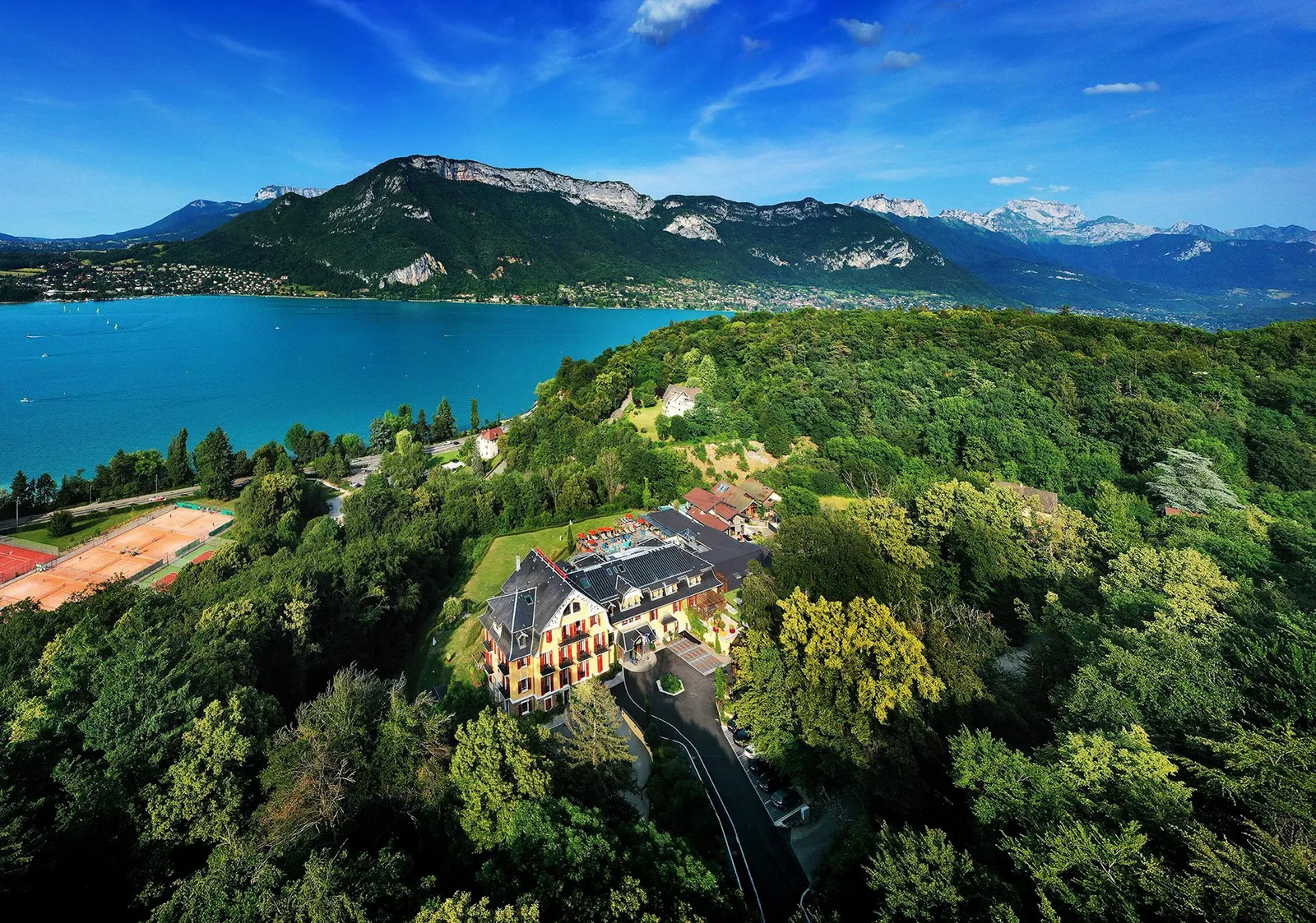Aerial view of Les Trésoms Lake and Spa Resort on its wooded hillside above Lake Annecy
