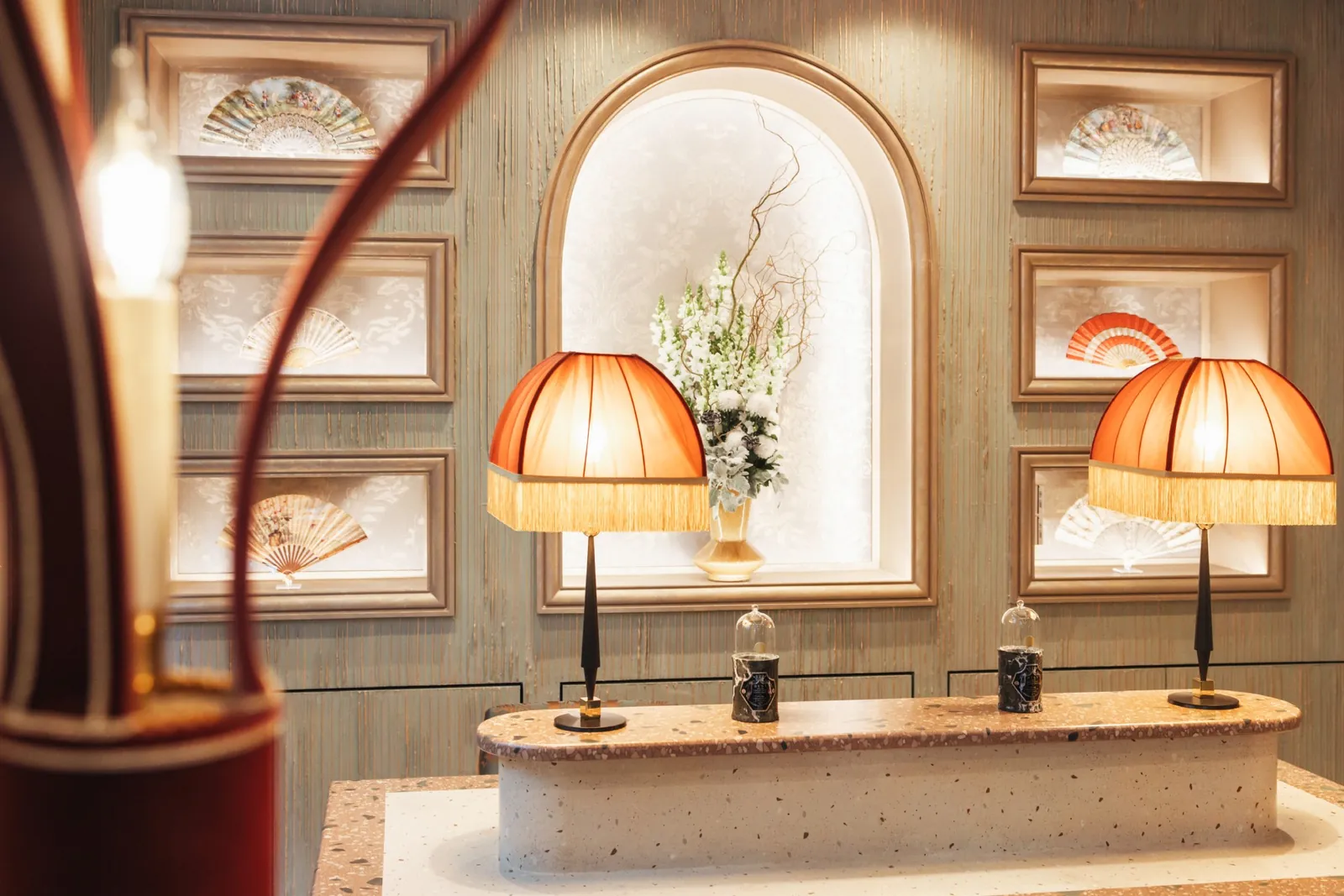 Reception area of Maison Barrière Vendôme with fringed table lamps, an arched niche and framed fans
