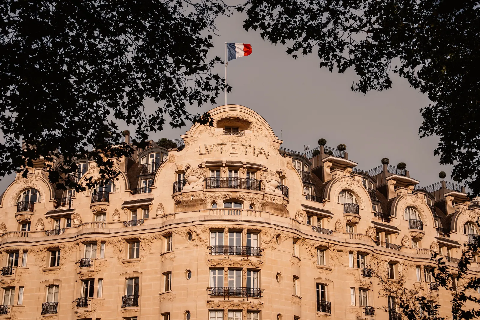 Haussmann-style stone facade with a French flag above the trees at Mandarin Oriental Lutetia, Paris