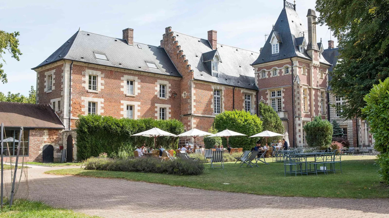 Red-brick manor with parasols on the terrace and a garden lawn at Manoir des Plaines Picardes, Oise