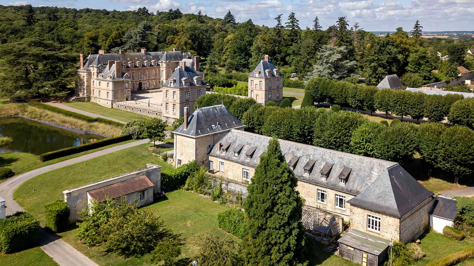 Manor house and outbuildings beside a pond and clipped hedges at Manoir des Prés Fleuris, Yvelines