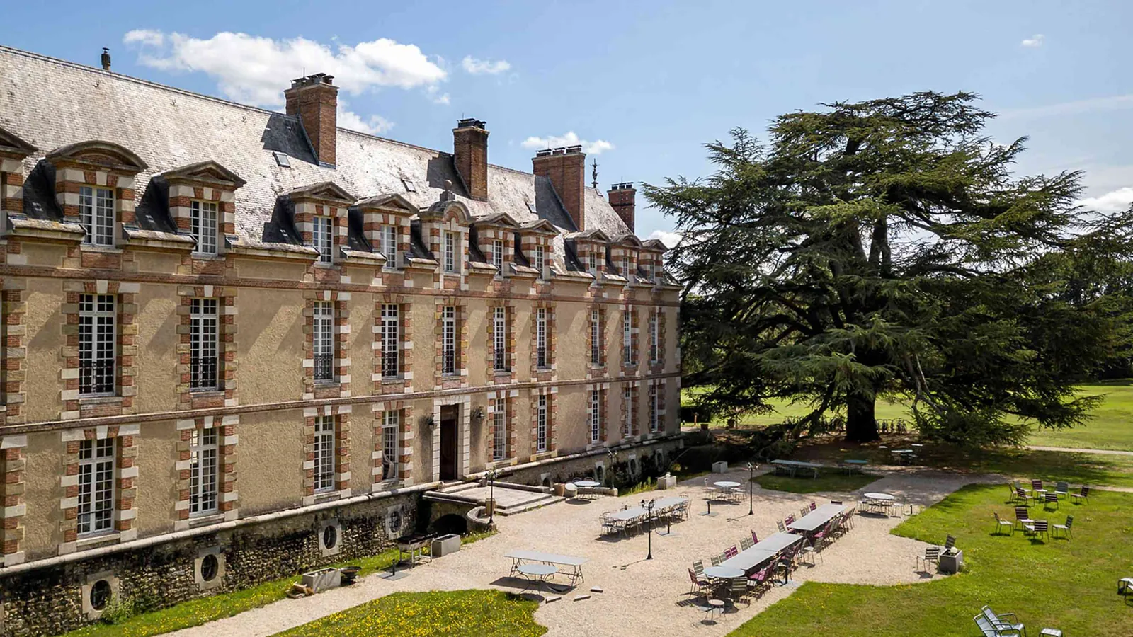 Stone manor facade with dormers and a large cedar tree at Manoir des Prés Fleuris, Yvelines