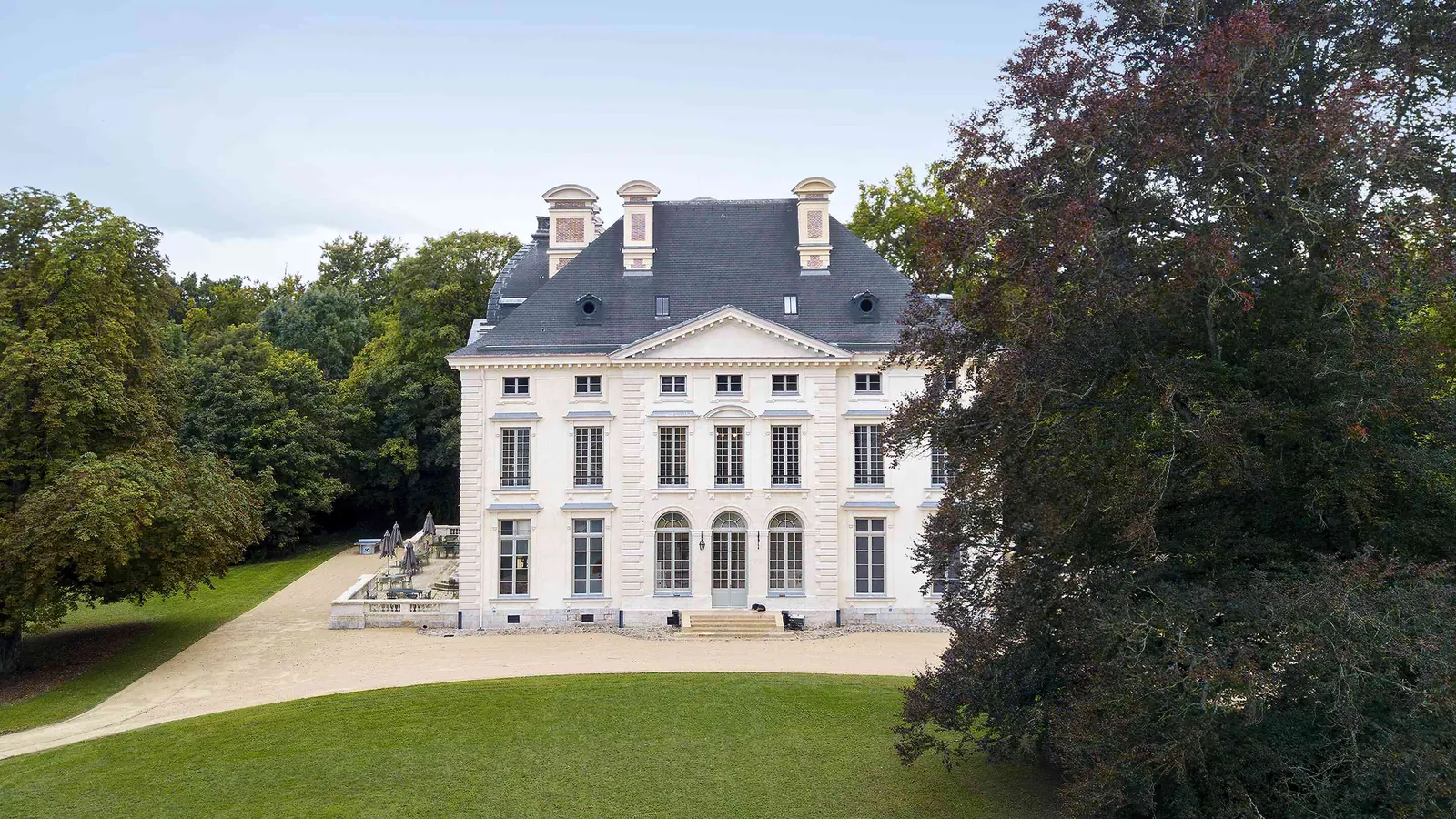 Stone château facade above a gravel courtyard with lawns at Manoir des Vallées Claires, Eure-et-Loir