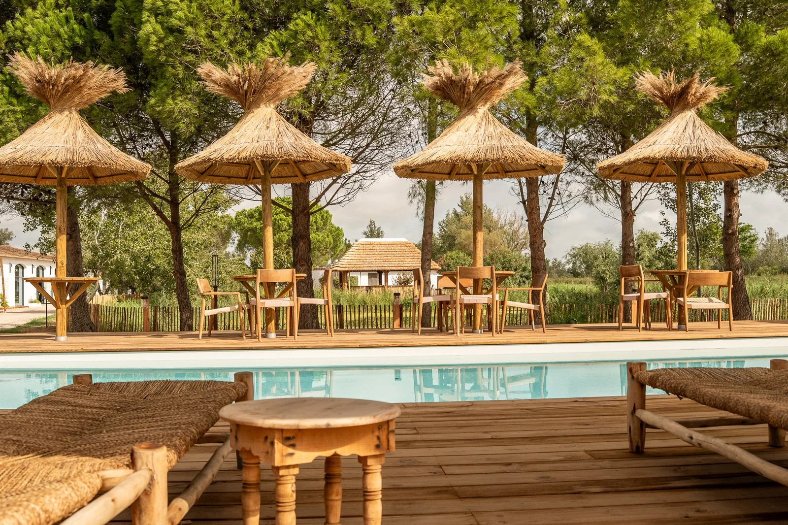 Pool terrace with reed parasols and tables among the pine trees at Mas de Dard