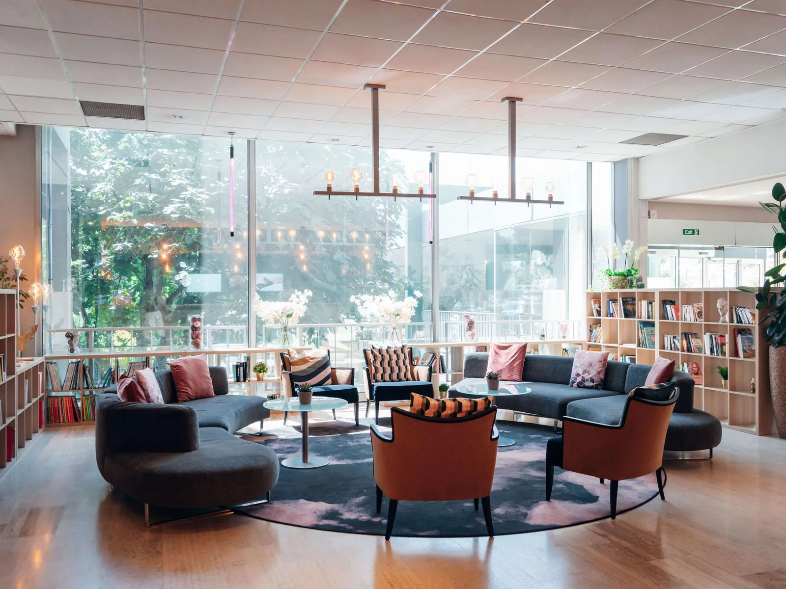 Lounge with dark sofas, armchairs and a library shelf beside large windows at Mercure Paris Orly Rungis