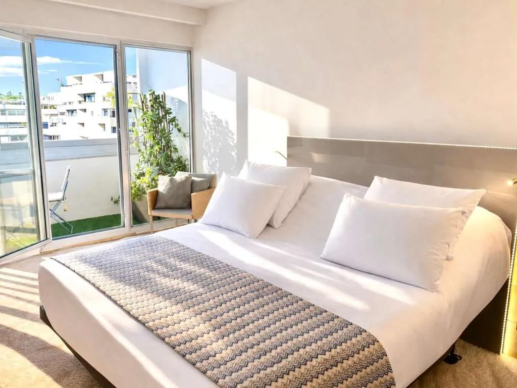 Bright room with balcony door, plant and grey-patterned throw on the bed at Mercure Paris Vaugirard, Paris 15e