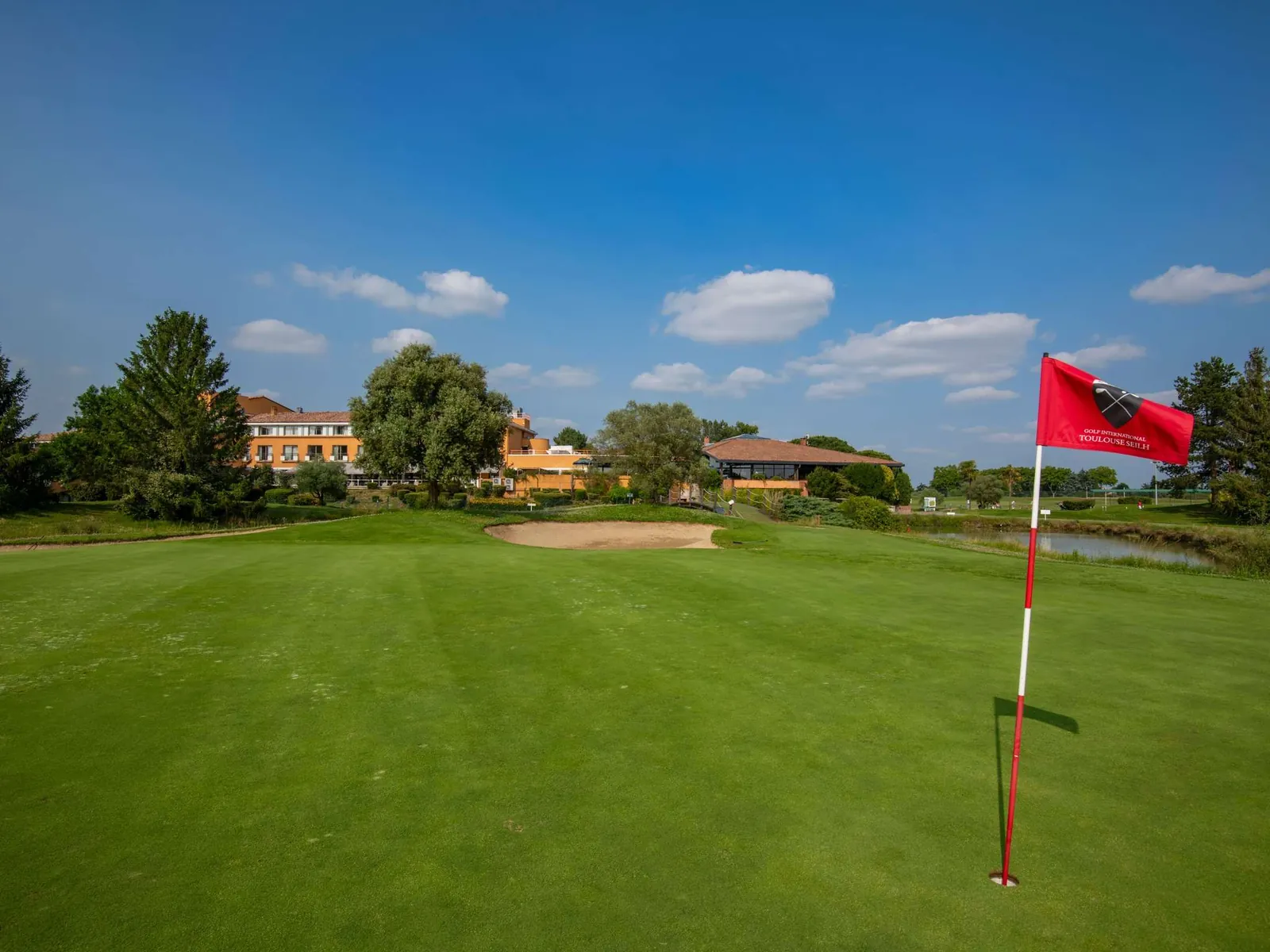 Golf green with a red flag and the hotel buildings beyond at Mercure Toulouse Aéroport Golf de Seilh