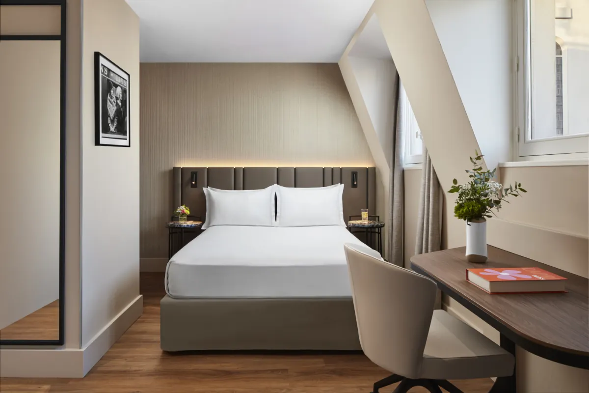 Standard guest room at the NH Paris Gare de l'Est with a made bed, a wooden desk and a grey armchair under the sloping roof
