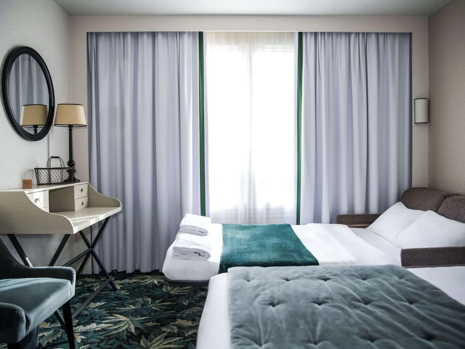 Guest room at the Novotel Domaine de Maffliers with a double bed, teal throw and writing desk