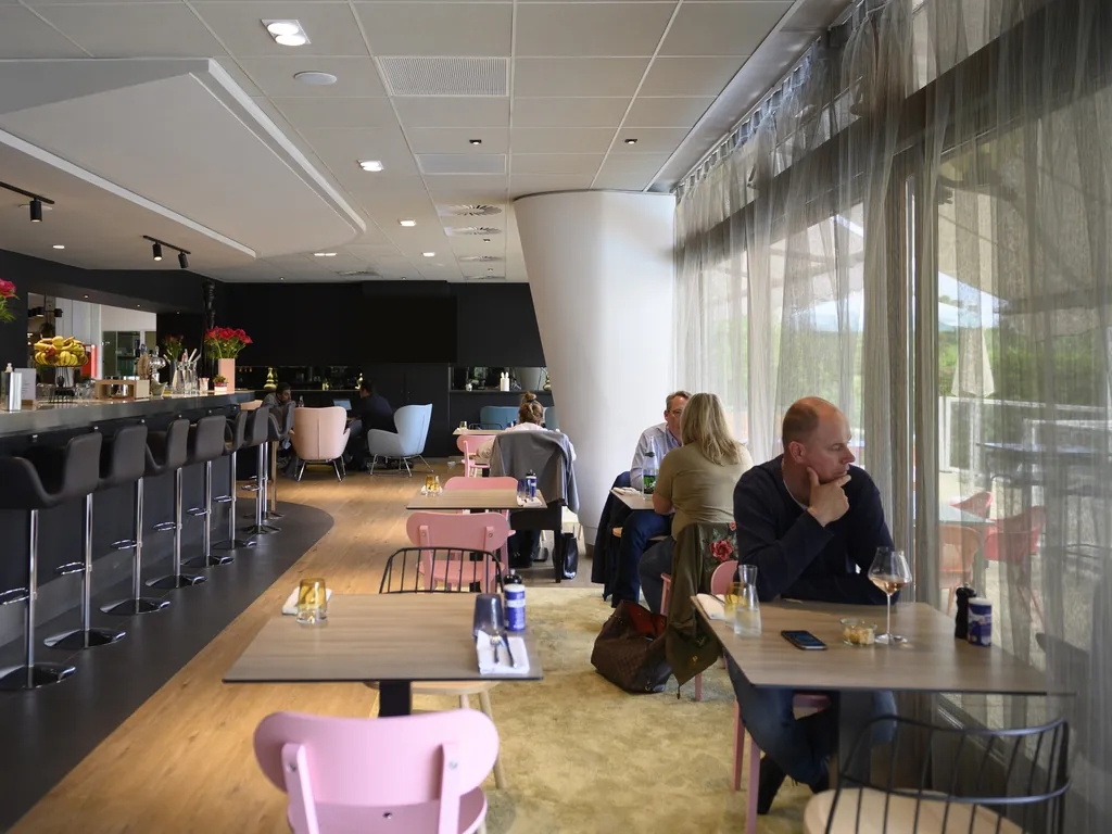 Bar lounge with high stools and pink chairs where guests relax at Novotel Paris Créteil Le Lac