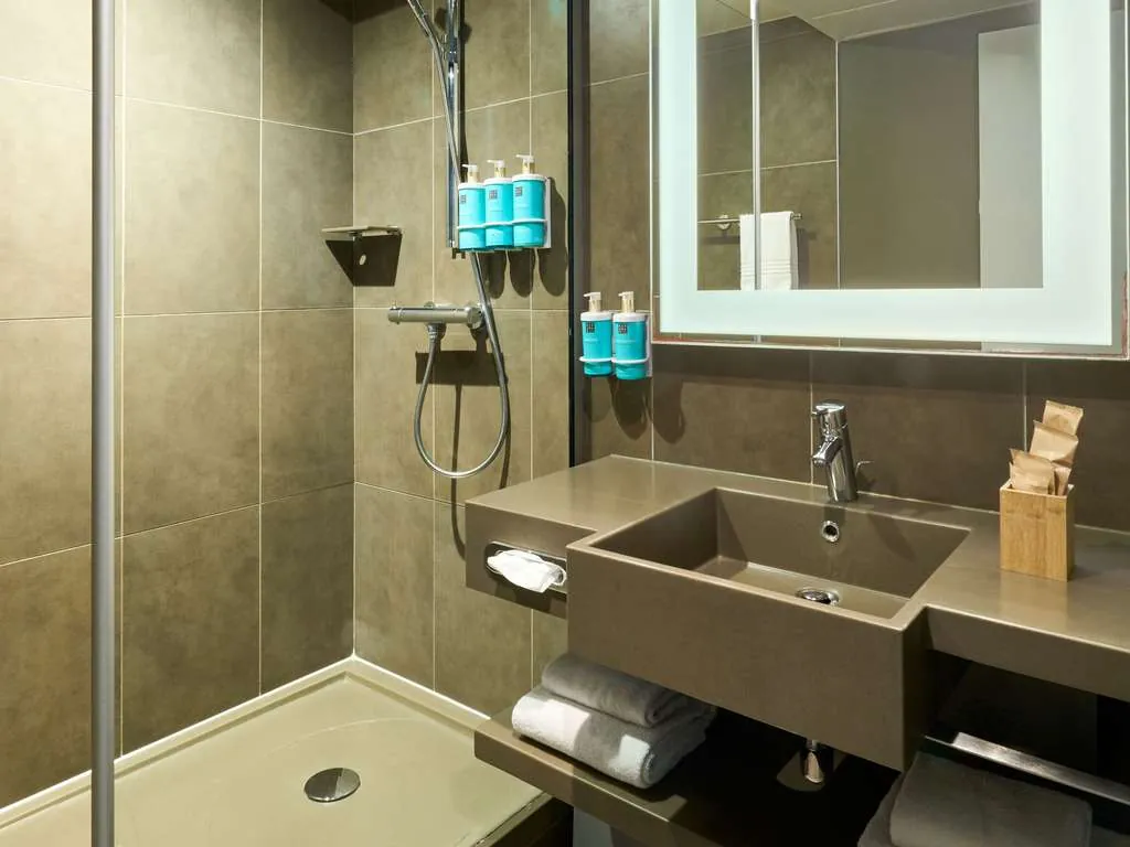 Bathroom with a walk-in shower, grey tiles and guest amenities at Novotel Paris La Défense Esplanade