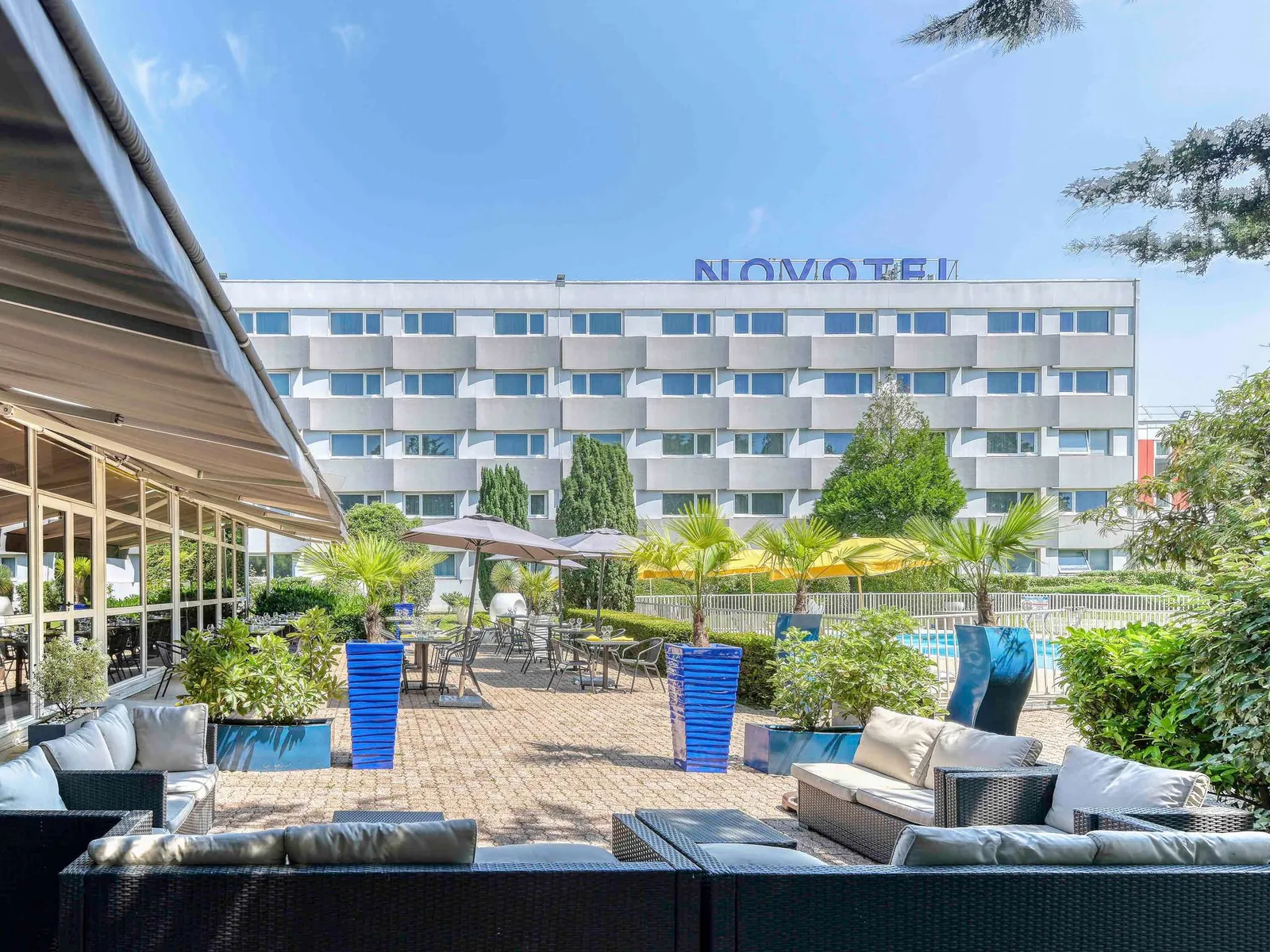 Outdoor terrace with lounge sofas and blue planters at Novotel Paris Nord Expo Aulnay