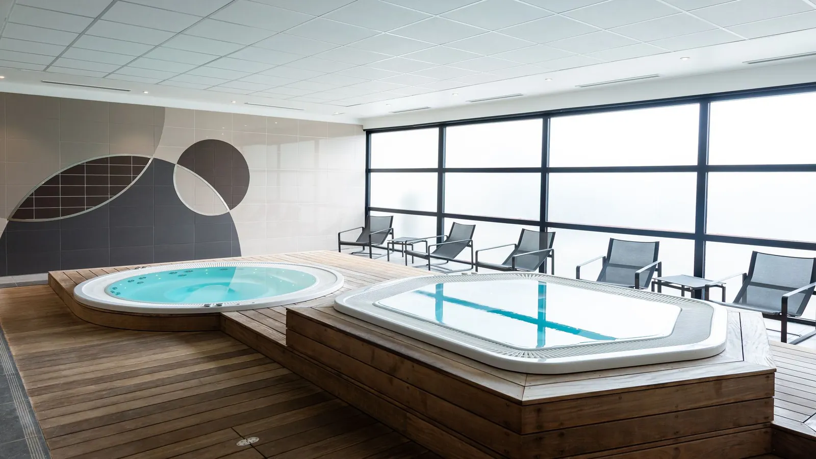 Indoor spa with a whirlpool and loungers beside large windows at Novotel Saint-Quentin Golf National