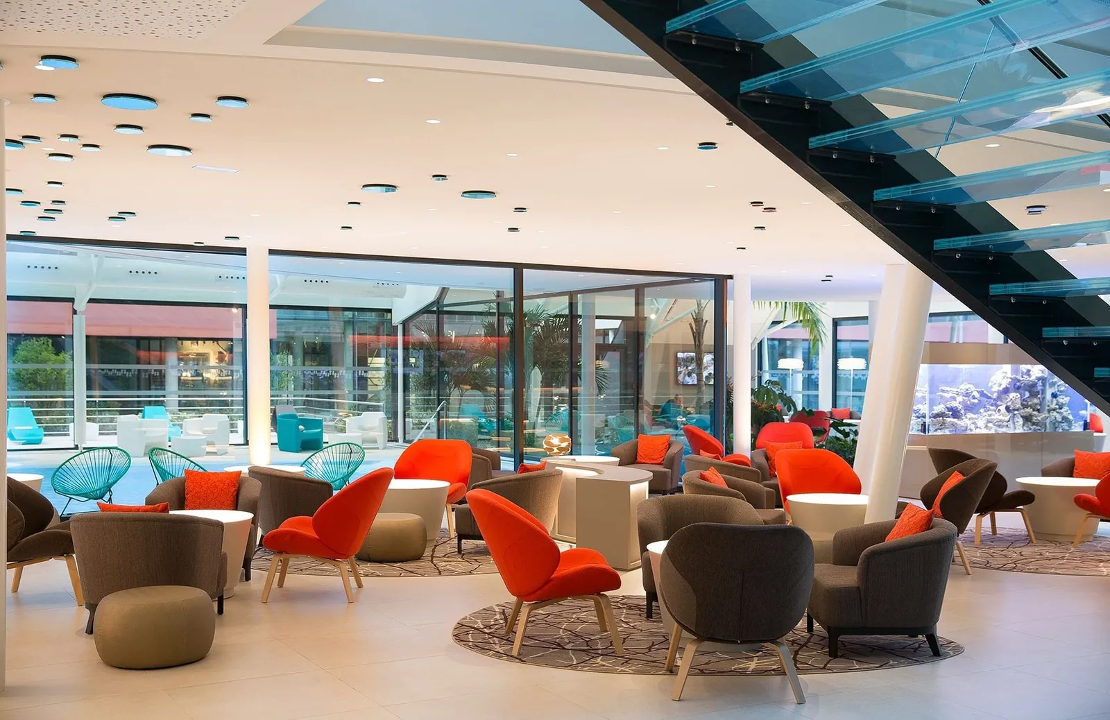 Lobby lounge of Oceania Paris Roissy CDG with orange armchairs and a glass staircase