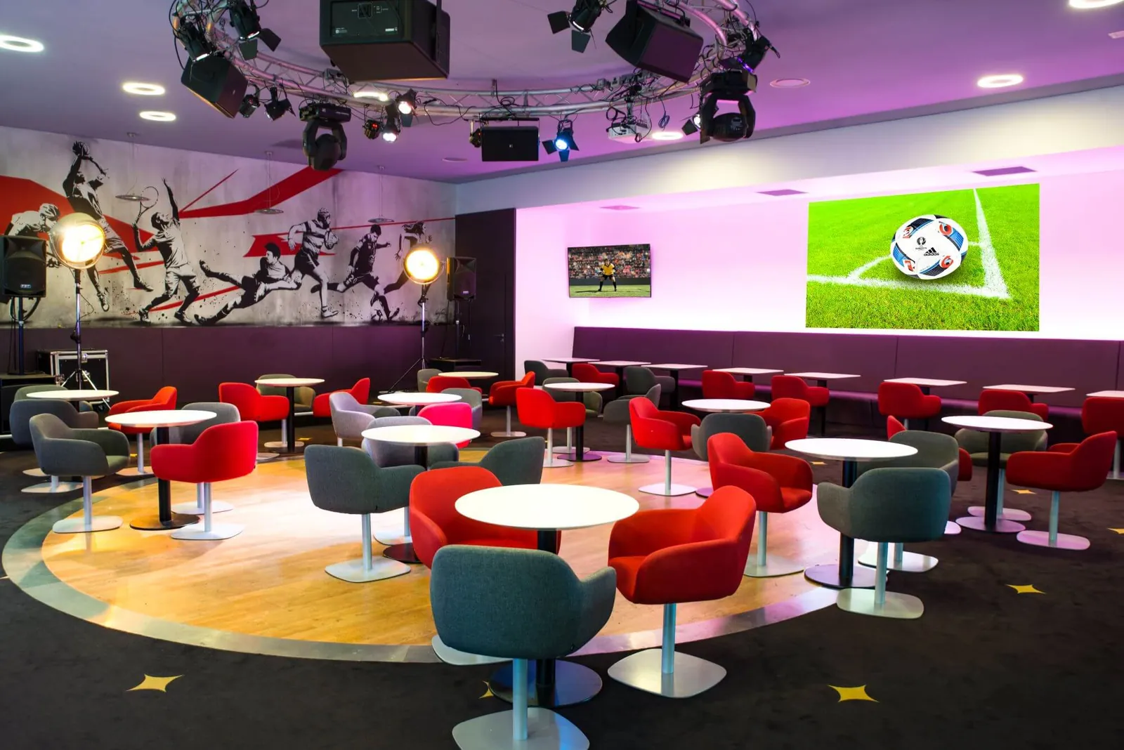 Café des Sports lounge at Resort Barrière Ribeauvillé with red and grey armchairs and a sports-themed mural