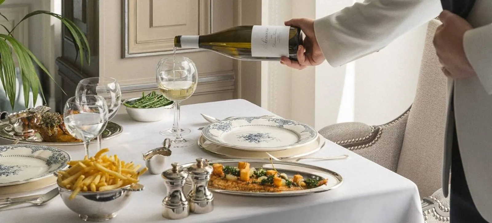 Restaurant table dressed with fine china, wine and fries as a waiter pours wine at Shangri-La Paris