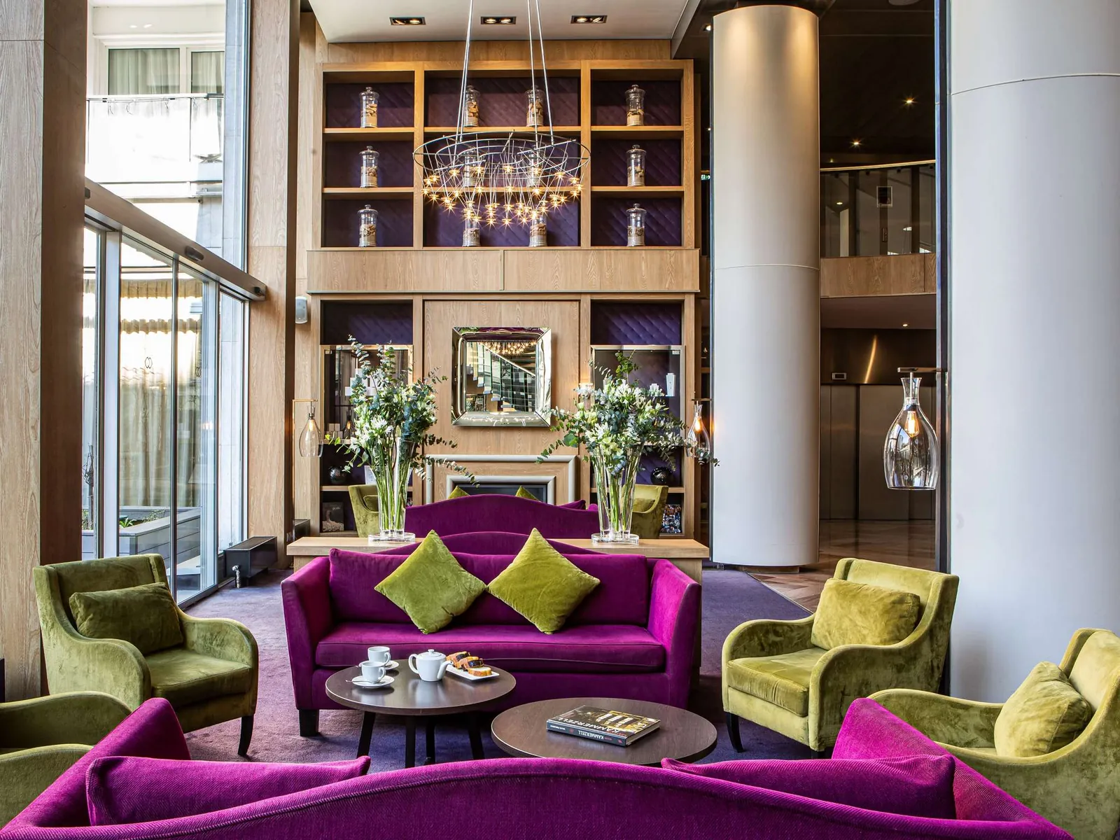 Lobby lounge with purple sofas, green armchairs and tall shelves at Sofitel Strasbourg Grande Île
