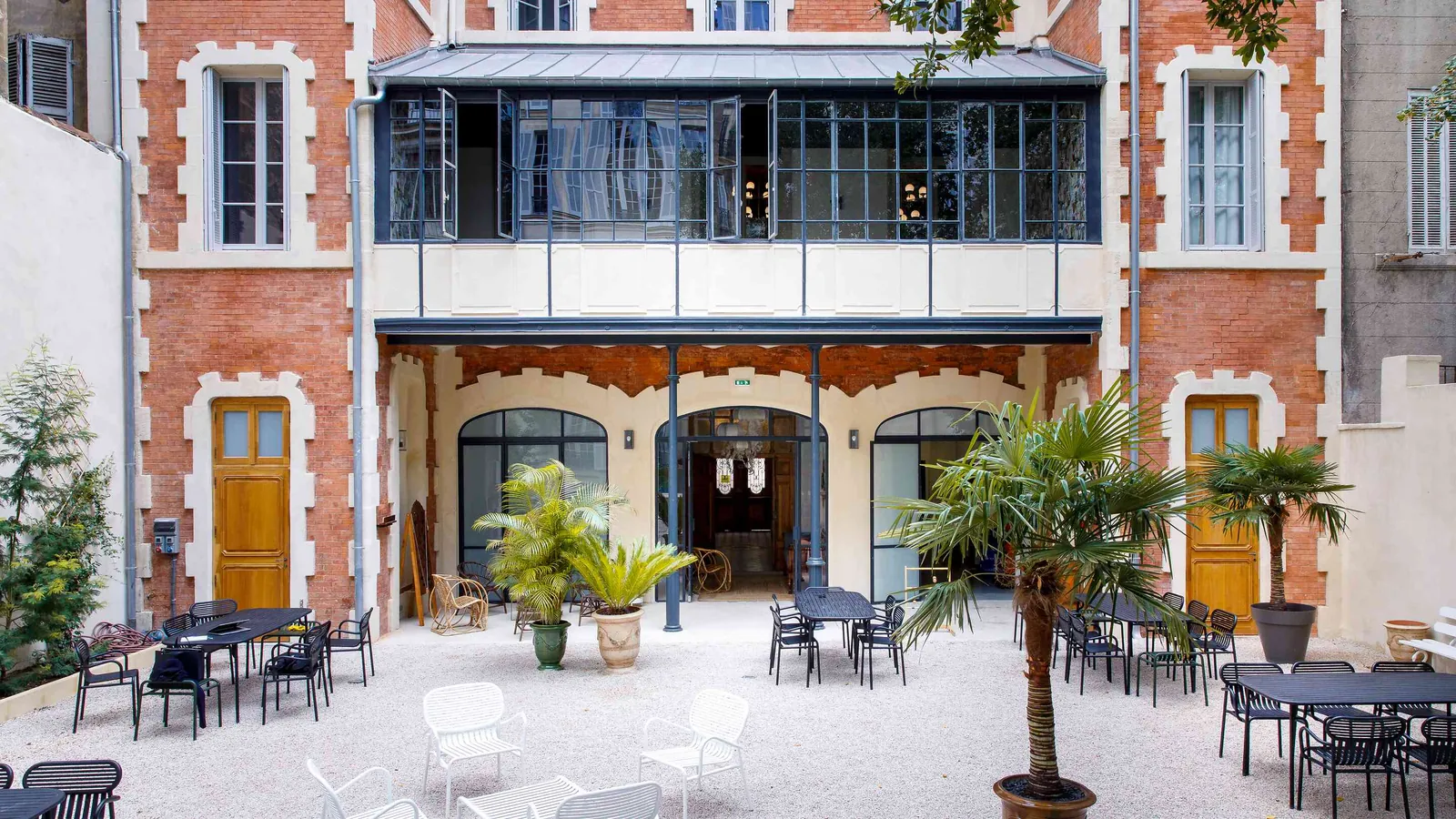 Brick courtyard with palm trees and café tables at Villa des Verrières in Marseille