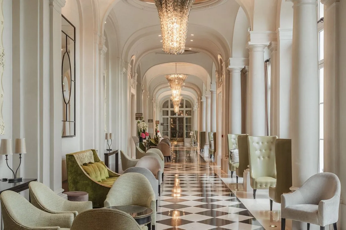 Gallery corridor with a checkered marble floor and armchairs at Waldorf Astoria Versailles - Trianon Palace