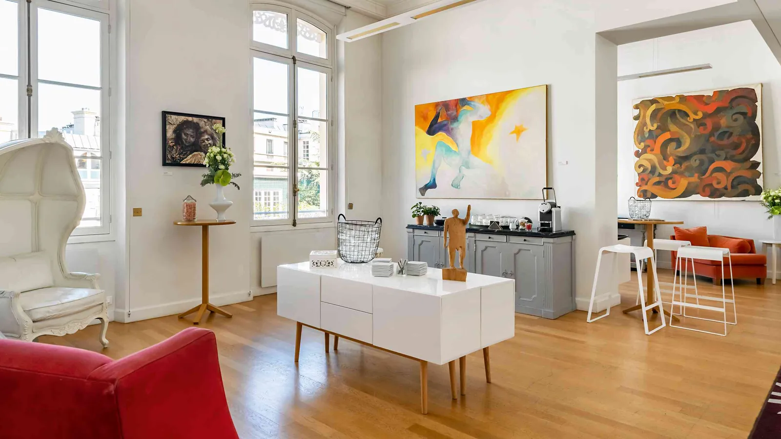 Light Atelier room with contemporary paintings, a white sideboard and high bar stools