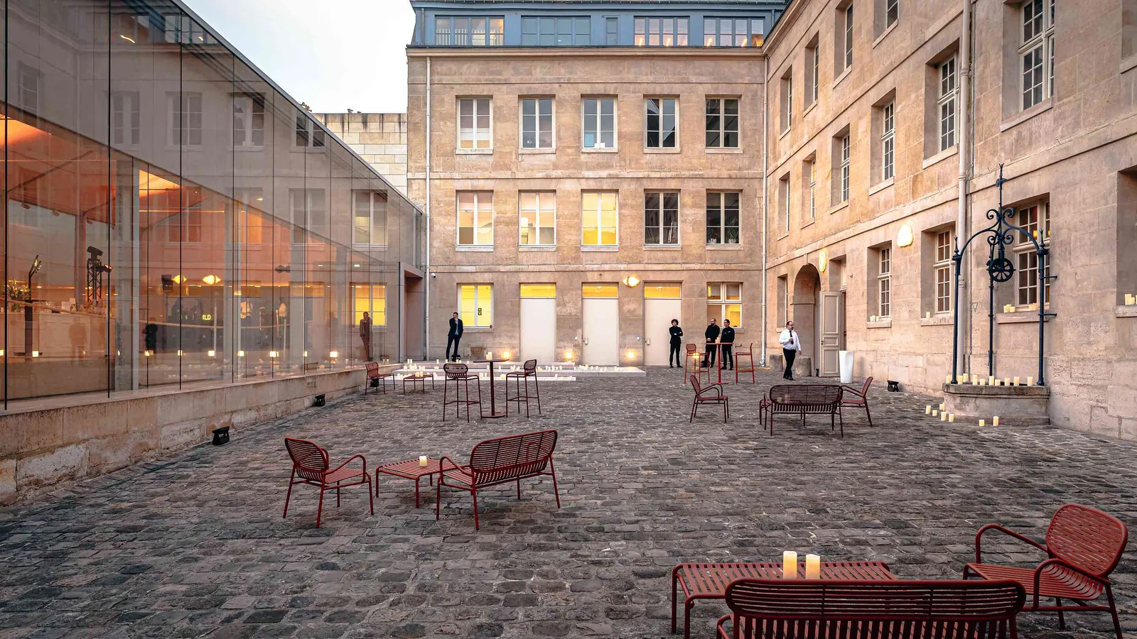 Left Bank Atrium courtyard with red garden chairs, a dusk-lit stone facade and glazed hall