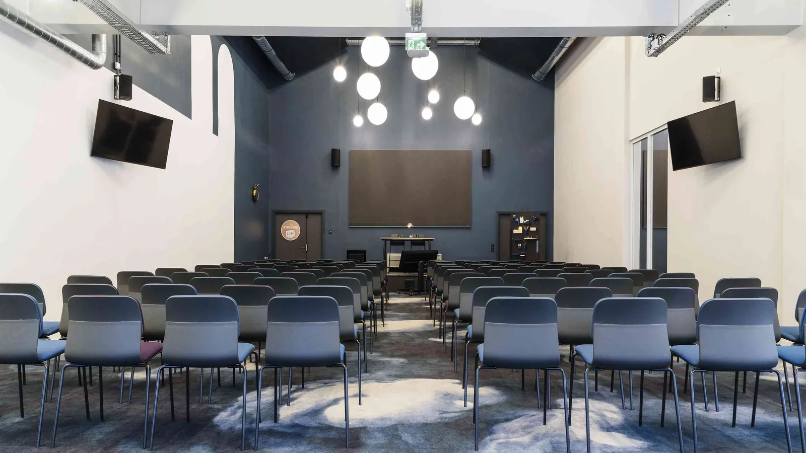 North Belvedere hall with classroom-style seating, wall-mounted screens and pendant lights