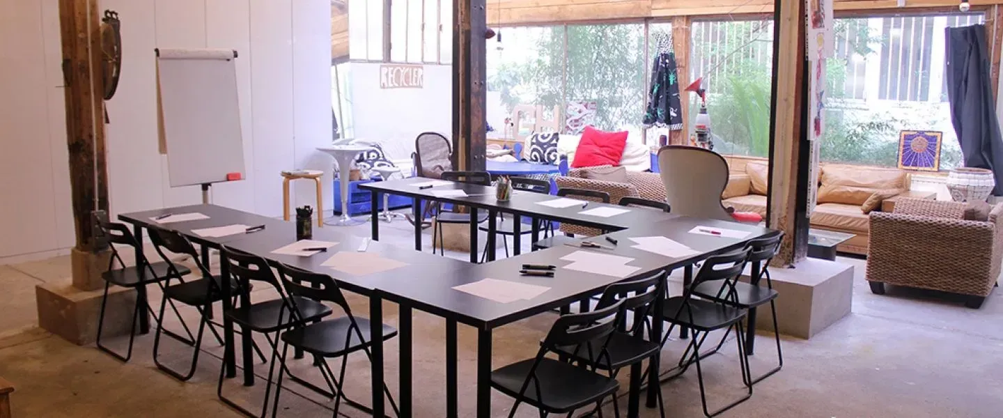 Long workshop tables with chairs in front of a glass wall and greenery