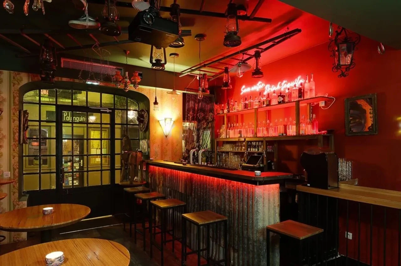 Bar with a red neon sign, a corrugated metal counter and high stools.