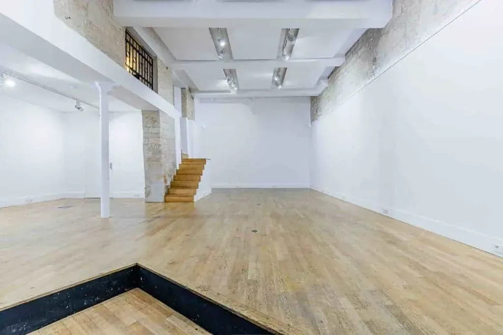 Room with a wooden floor, a staircase and a wall of tall windows