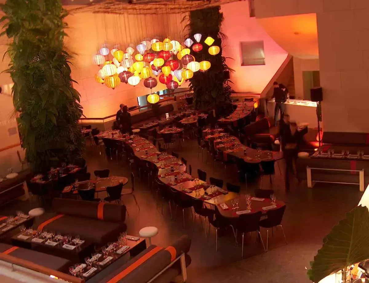 Dining tables and a glass chandelier in a warm-lit hall with plants