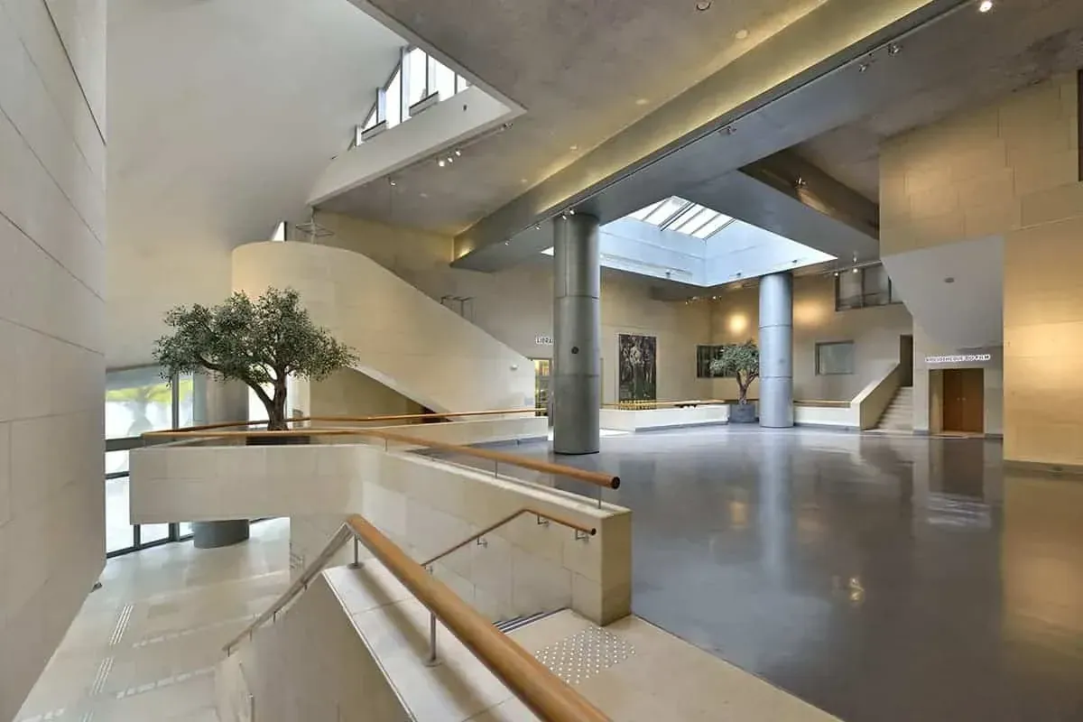 Glass-roof atrium with a curved stone staircase, columns and a grey floor