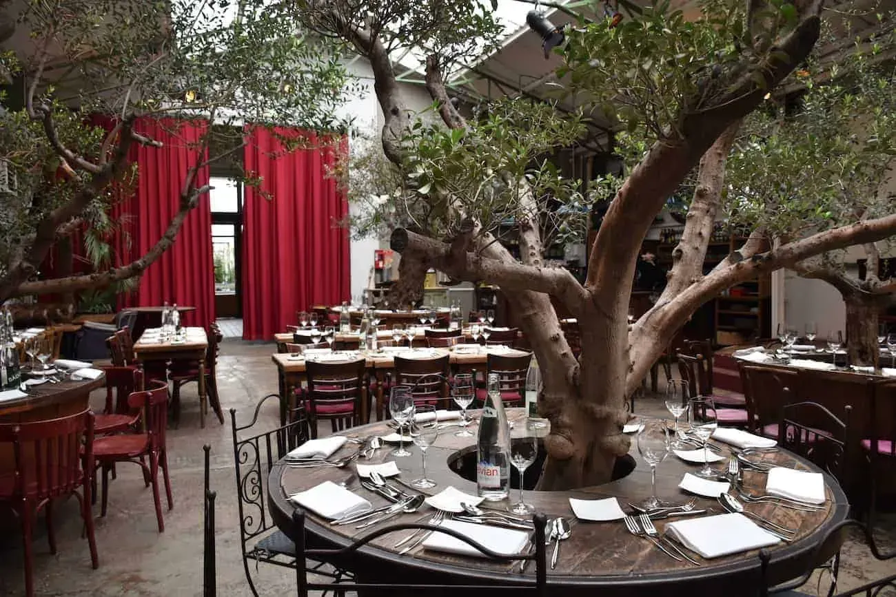 Industrial hall with a glass roof, olive trees and round dining tables
