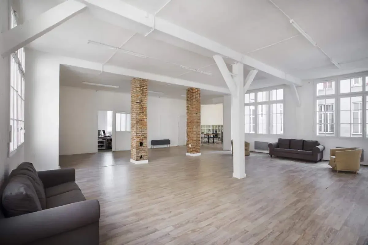 Loft with brick columns, white beams, large windows and sofas on a wooden floor
