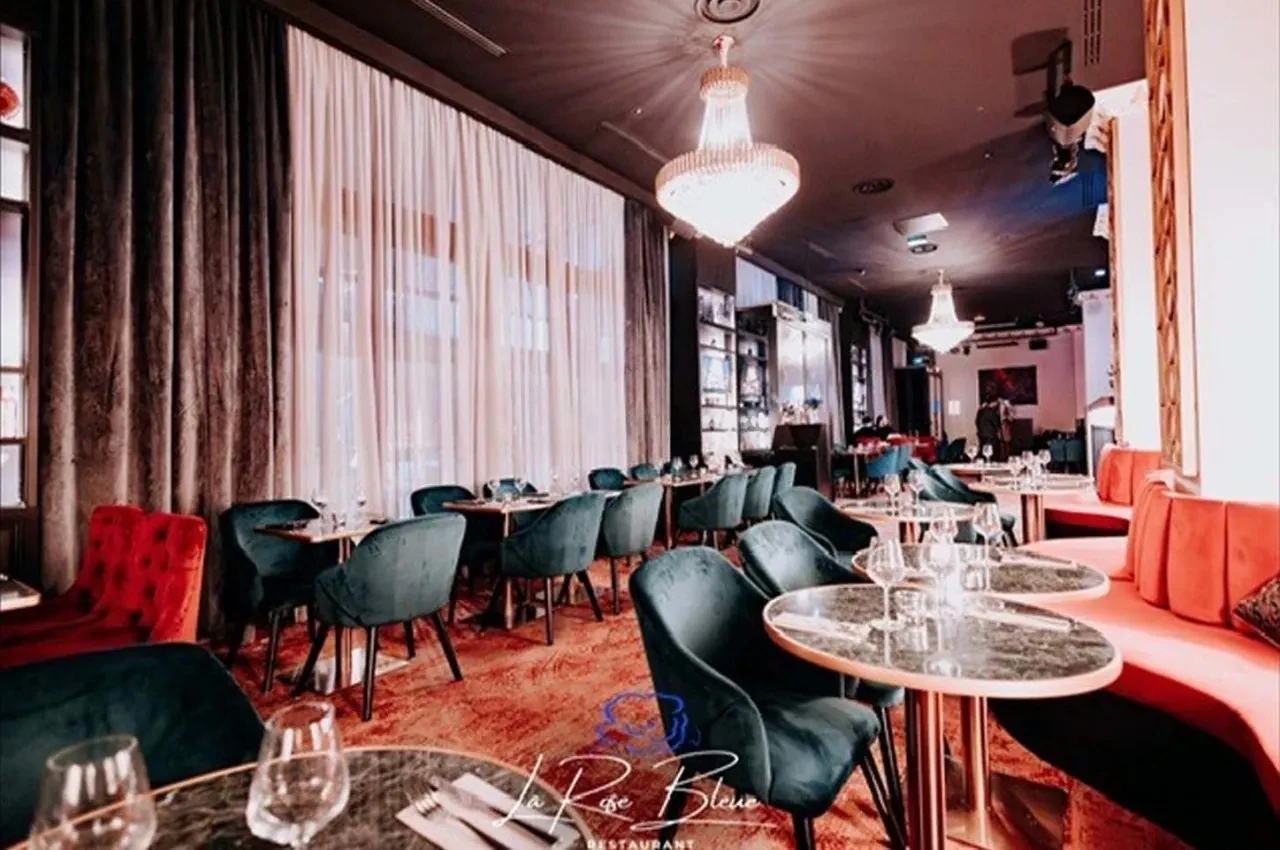 Restaurant room with a crystal chandelier, green velvet chairs and marble tables.