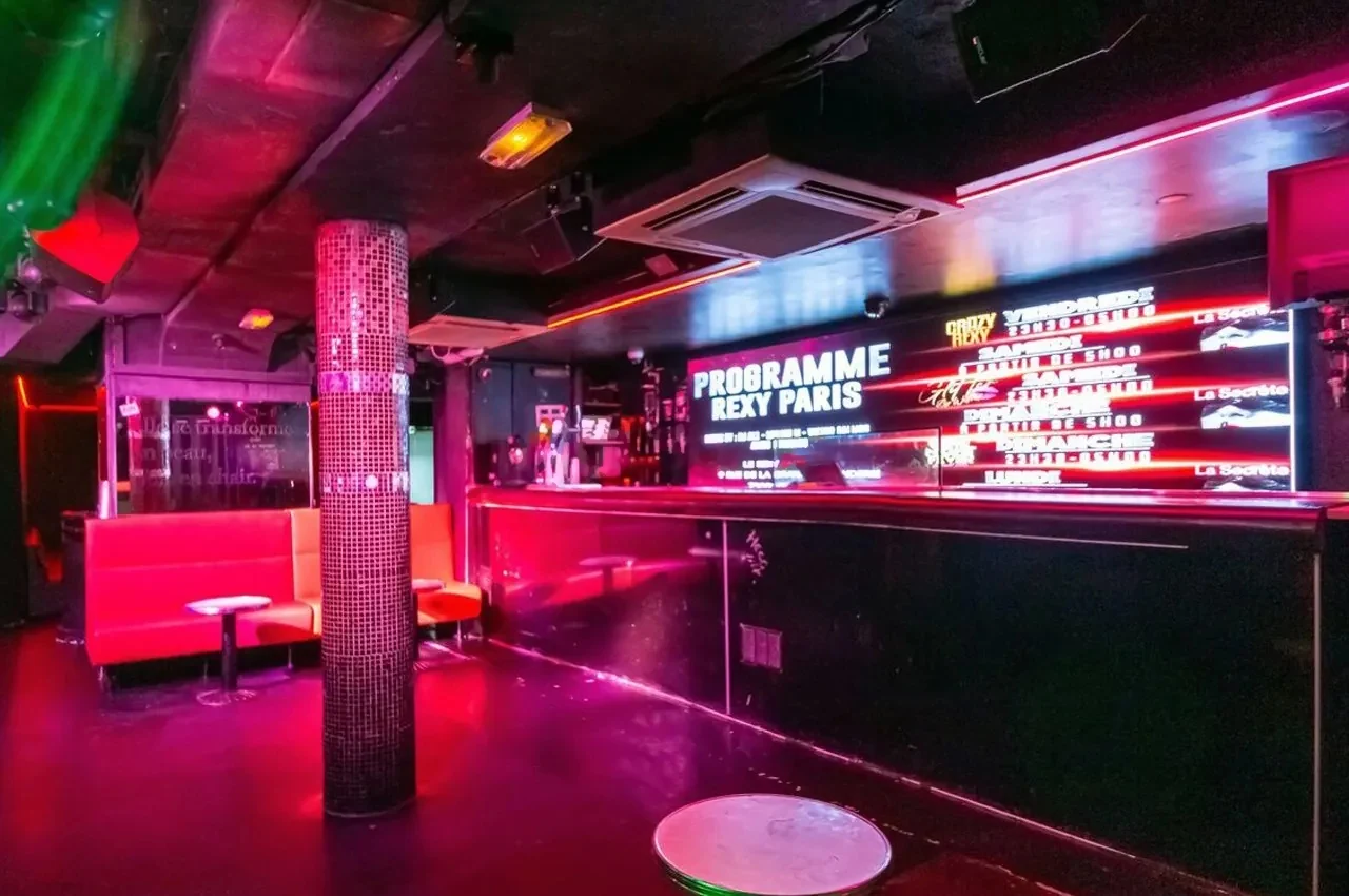 Lounge area with red banquettes, a mosaic-tiled pillar and an illuminated programme screen.