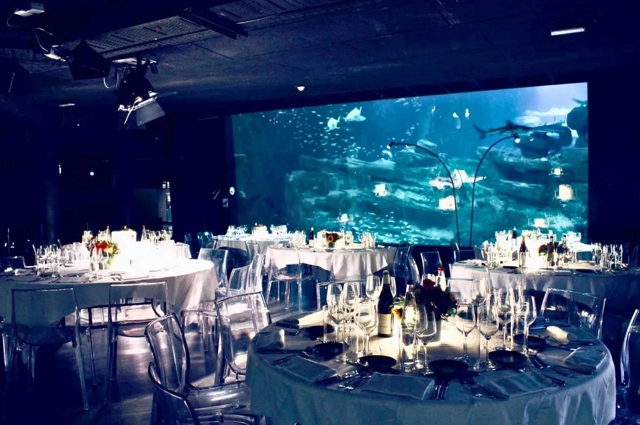 Round tables set for dinner beside a large illuminated tank