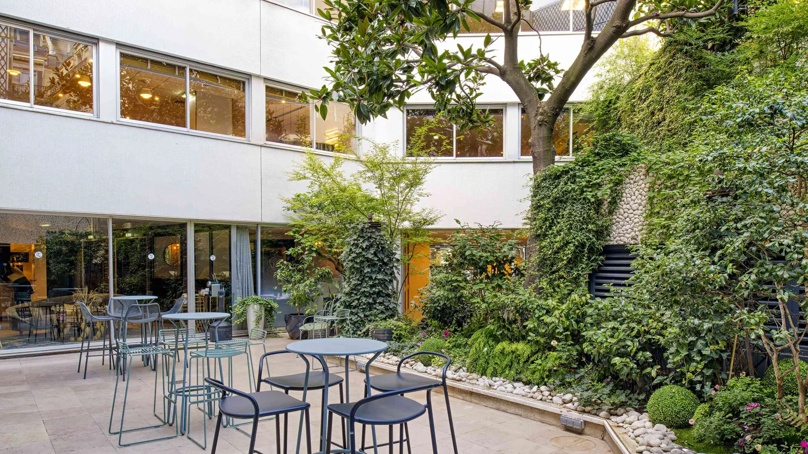 Golden House courtyard with a planted wall, bistro tables, bar stools and daylight