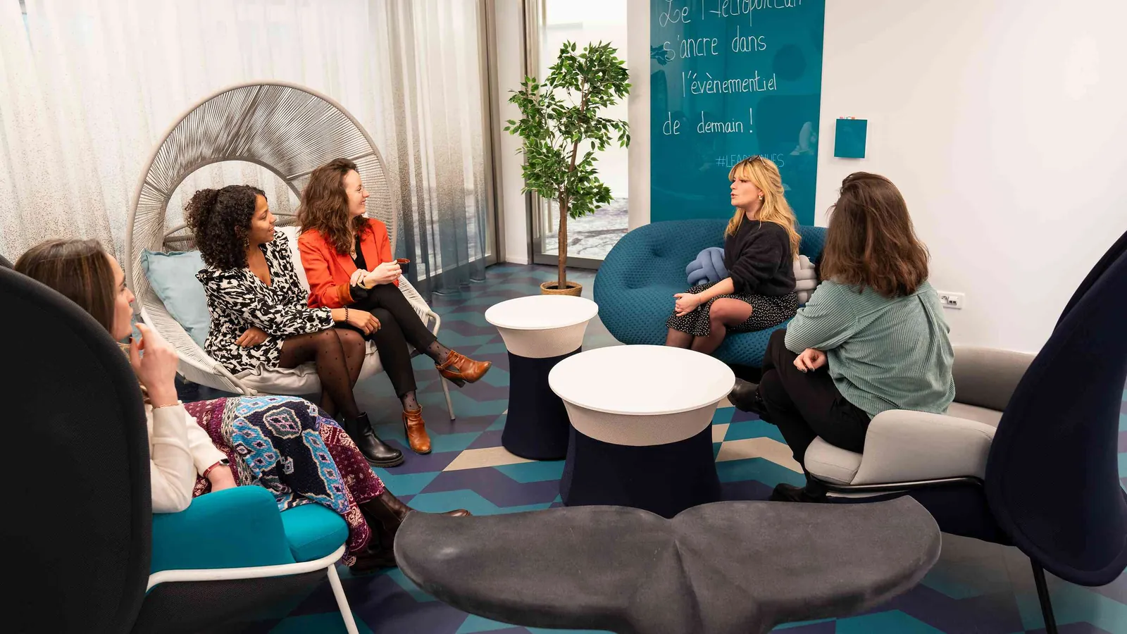 Contemporary Pavilion lounge with teal armchairs, grey pouffes and a potted tree