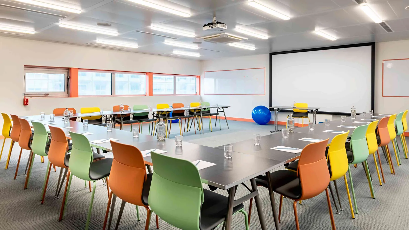 West Pavilion plenary room with orange, green and yellow chairs around long tables