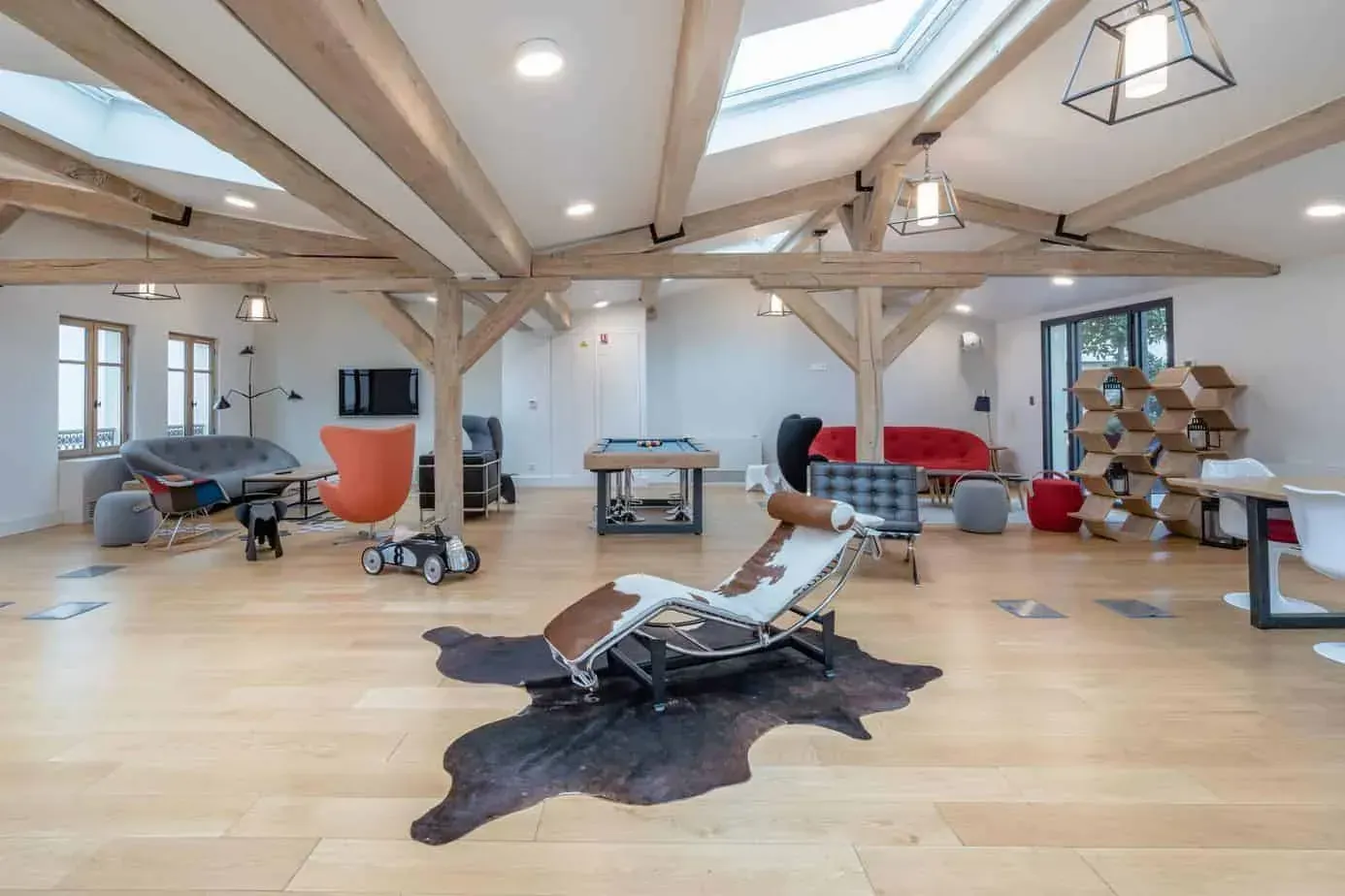 Large room with exposed timber beams, skylights and a lounge chair on a cowhide rug