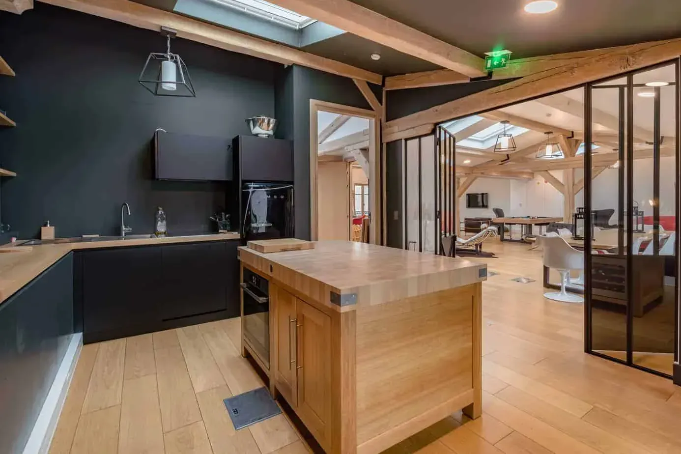 Open kitchen with dark cabinets and a timber island next to glass partitions