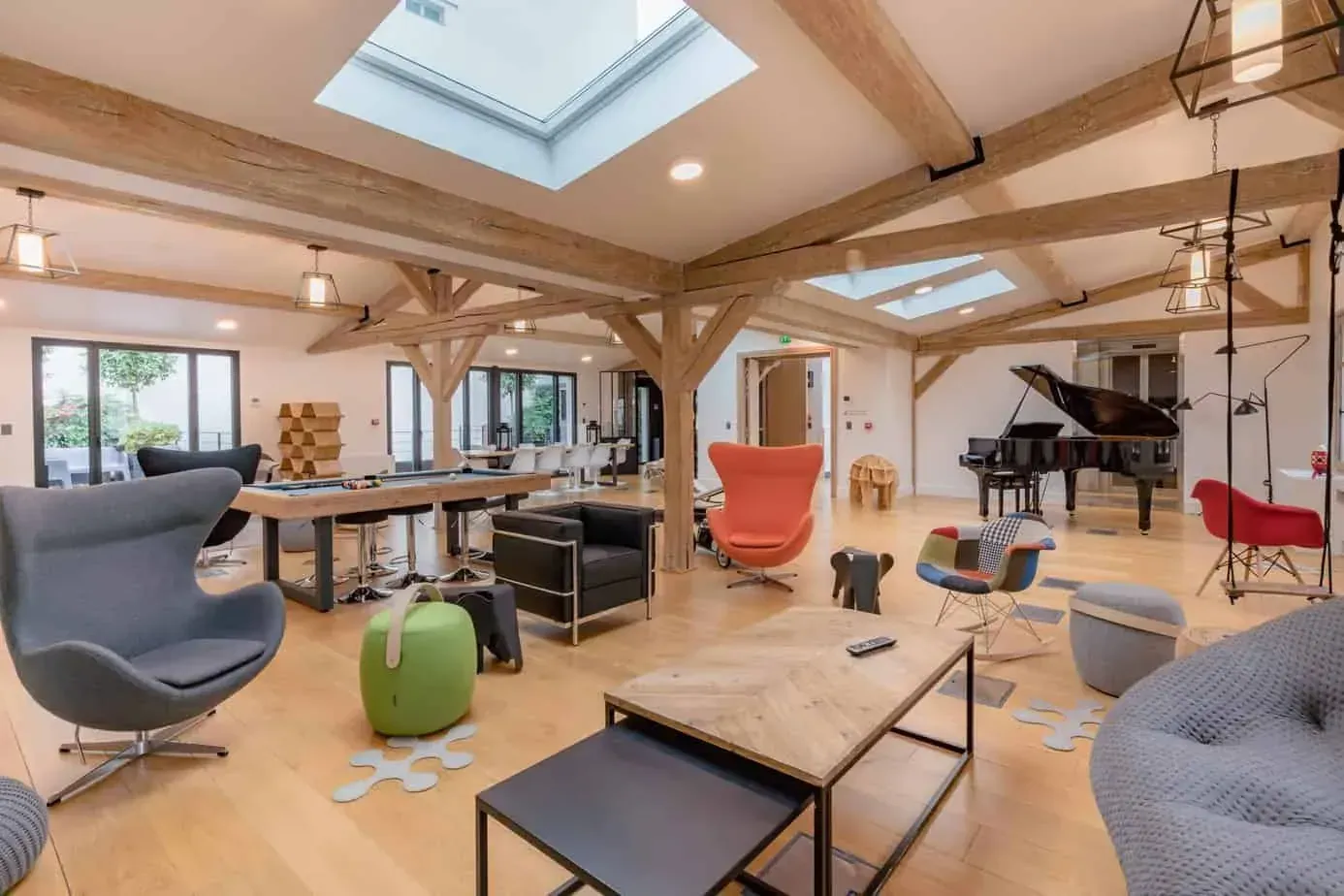 Lounge area with armchairs, a grand piano and low tables under timber beams